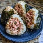 A hand holding a spicy tuna onigiri wrapped with nori seaweed.